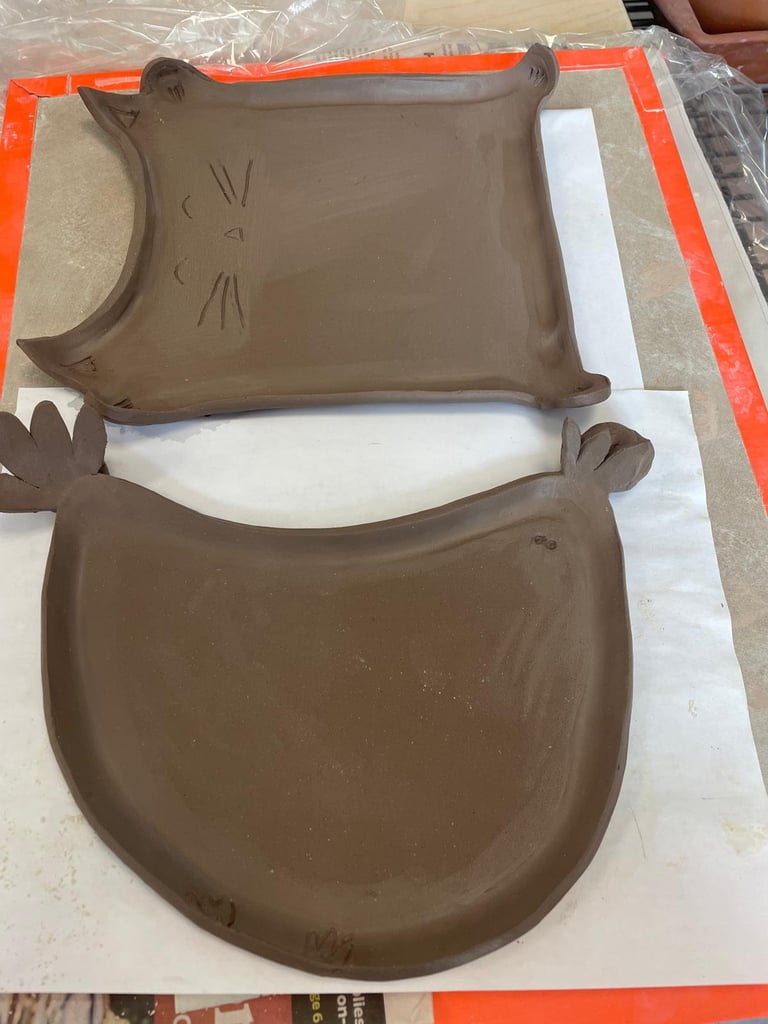 Two brown clay cat-shaped dishes with whisker markings on white paper with orange border frame