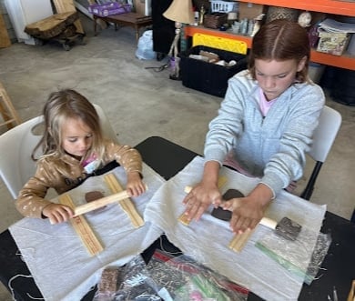 Two children working on a newspaper project together at a table in a workshop or classroom setting