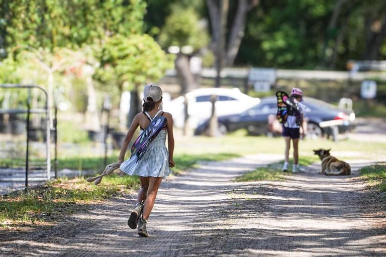 Young girl jogging on a tree-lined park path with other children visible in the background