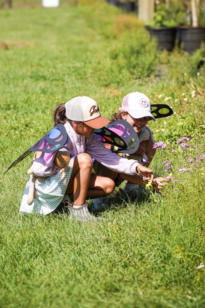 Two young children in baseball caps examining flowers in a grassy outdoor area