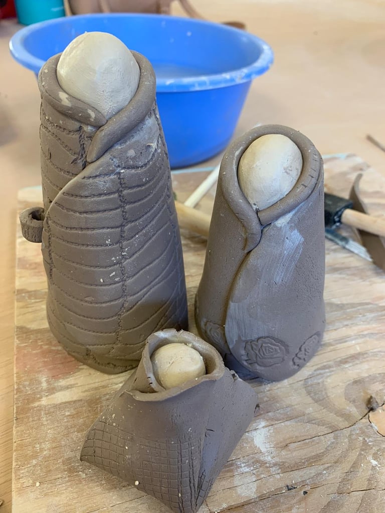 Three clay sculpture forms with white spheres inside, displayed on a wooden surface with a blue bowl in the background