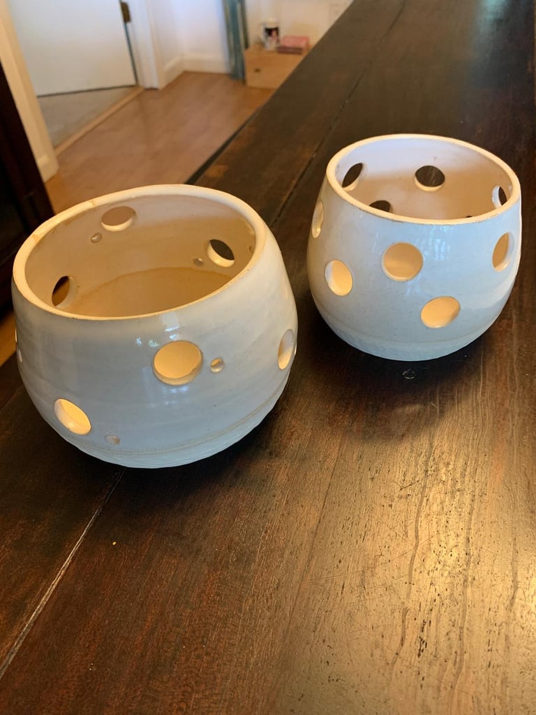 Two white ceramic bowls with circular cutout patterns on a dark wooden floor indoors