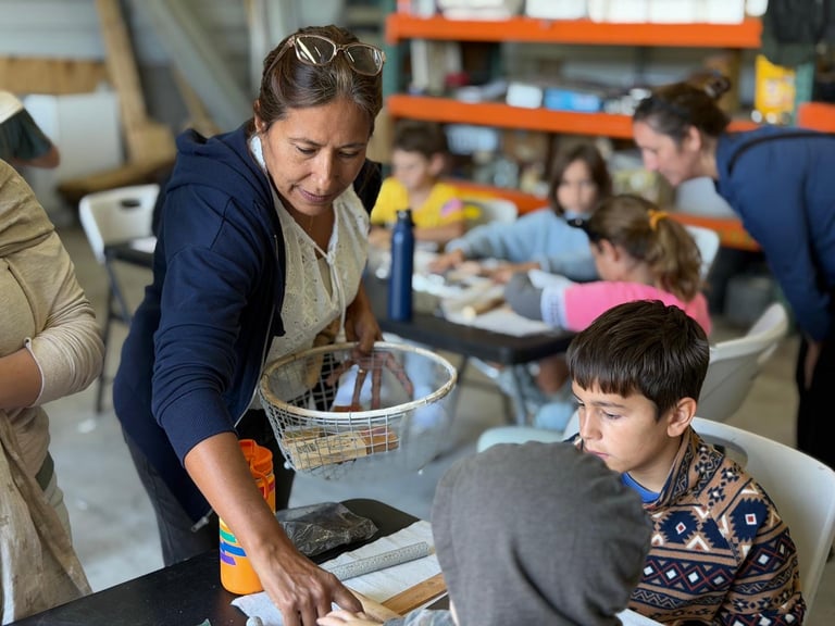 Art teacher instructing a group of young children at tables during a classroom activity in a bright studio space