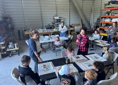 Art class in a workshop studio with students seated at tables and an instructor demonstrating techniques to the group