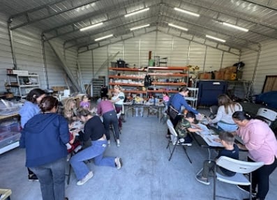 Group of people sitting and standing in a large warehouse space with shelving, working or volunteering together