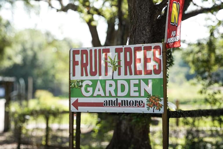 Roadside sign for Fruit Trees Garden and More, mounted on a tree with green orchard landscape in the background