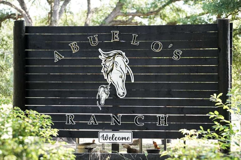 Black wooden ranch sign with horse illustration and Bulos Ranch text, surrounded by greenery and trees