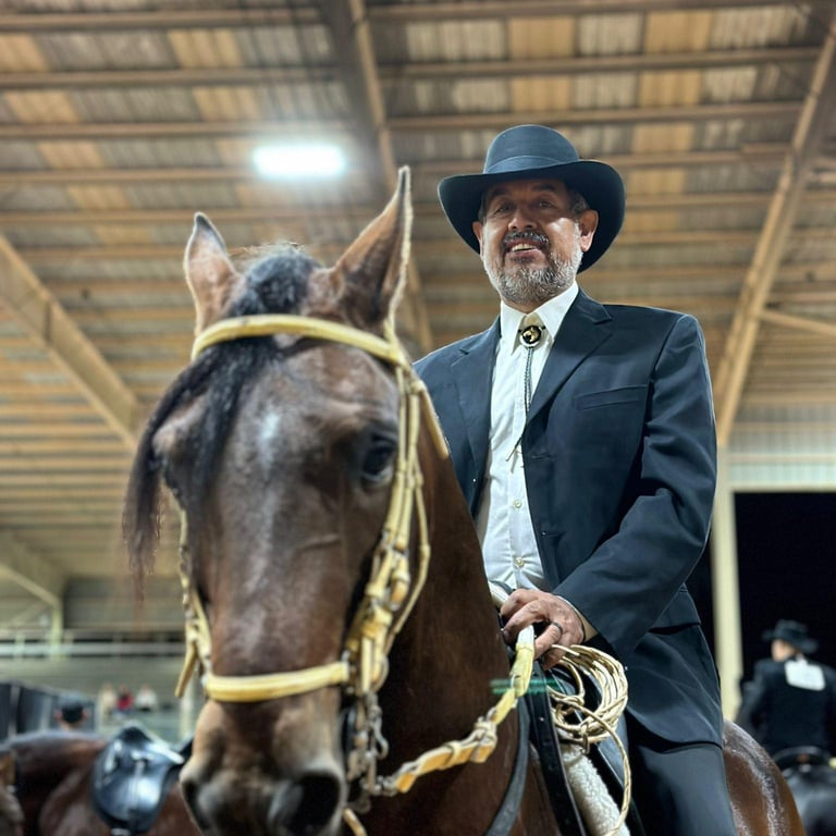 Man in cowboy hat and dark suit leading a brown horse with yellow halter in an indoor arena